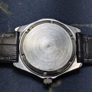 May include: Close-up of the back of a silver-toned wristwatch with a black leather band. The watch face is a brushed metal with a circular design. The band is black and textured.
