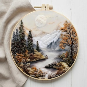 May include: A detailed embroidery landscape scene in a round wooden hoop. The artwork depicts a serene mountain and river scene with trees in shades of green, brown, and orange. A full moon is visible in the sky, and the overall color palette is muted.