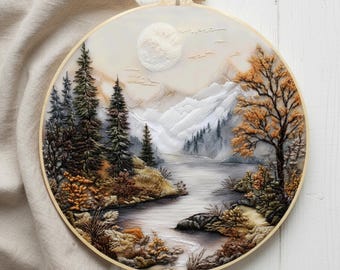 May include: An embroidered landscape scene in a round wooden hoop. The artwork shows a mountain and river scene with trees in green, brown, and orange hues. A full moon is visible in the sky, and the overall colour palette is muted and natural.