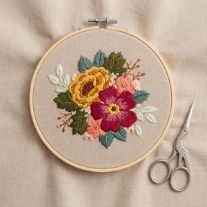 May include: A circular wooden embroidery hoop containing beige fabric with a hand-stitched floral design featuring a large mustard yellow flower, a deep magenta flower, and smaller pink blossoms surrounded by dark green and sage leaves.