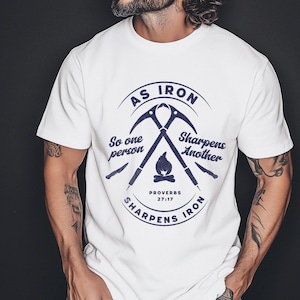May include: White t-shirt with a navy blue graphic design. The design includes crossed ice axes, a campfire, and text that reads "As Iron Sharpens Iron" and "Proverbs 27:17".