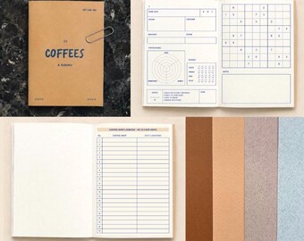 Puede incluir: Un cuaderno color canela con el texto 22 COFFEES & SUDOKU en la portada. Las páginas interiores presentan plantillas impresas en azul para notas de cata de café, un sudoku y un registro numerado para veintidós visitas a cafeterías.