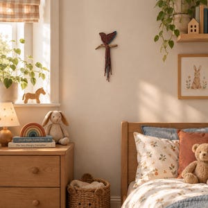 May include: A macrame wall hanging of a bird perched on a branch, featuring intricate knotted cord work in shades of red, blue, and brown. The bird has a rounded body and a long, trailing tail made of multiple strands of hanging cord.