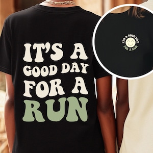 Könnte beinhalten: Schwarzes T-Shirt mit dem Text "IT'S A GOOD DAY FOR A RUN" in Weiß und Grün. Eine kleinere kreisförmige Grafik auf der rechten Seite zeigt ein lächelndes Gesicht mit dem Text "IT'S A GOOD DAY FOR A RUN".
