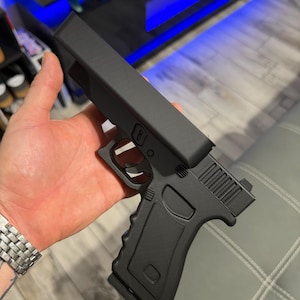 May include: A matte black toy pistol featuring a solid, blocky slide design, a textured grip, a trigger guard, and a trigger. The object has a simplified, non-functional appearance with clean lines and a uniform dark finish throughout the frame.