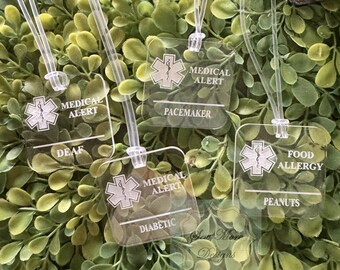 May include: Four clear plastic medical alert tags with a red star of life symbol and text. The tags read "Medical Alert", "Pacemaker", "Deaf", "Diabetic", "Food Allergy", and "Peanuts".