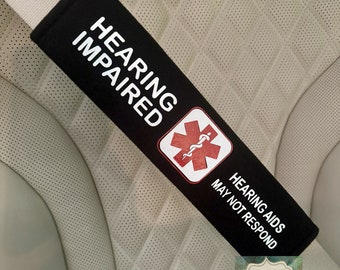May include: Black and white seatbelt cover with the text "Hearing Impaired" and a red medical symbol. The text "Hearing Aids May Not Respond" is also printed on the cover.