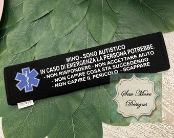 May include: Black wristband with a white star of life symbol and text in Italian that reads "MINO - SONO AUTISTICO IN CASO DI EMERGENZA LA PERSONA POTREBBE. - NON RISPONDERE - NON ACCETTARE AIUTO - NON CAPIRE COSA STA SUCCEDENDO - NON CAPIRE IL PERICOLO - SCAPPARE" and the text "Sew More Designs".