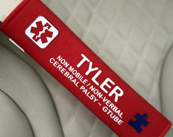 May include: Red seatbelt cover with the name "TYLER" and the text "NON MOBILE / NON-VERBAL CEREBRAL PALSY ~ GTUBE". A blue puzzle piece is in the bottom right corner. A medical symbol is in the top left corner.