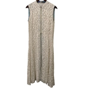 May include: A sleeveless, floor-length dress in a cream color, featuring a delicate, all-over floral pattern. The dress has a high, mandarin collar and a full-length zipper down the front. The dress is hanging on a wooden hanger.