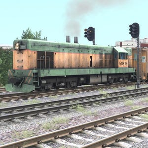 May include: A green and tan diesel locomotive pulling a series of brown freight cars on a railroad track. The train is moving along a track with signals and a light blue sky in the background. Smoke rises from the locomotive.