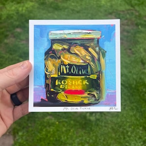 May include: An original painting of a jar of Mt. Olive Kosher Dill pickles. The jar is filled with yellow-green pickles and has a green and white lid. The label reads "Mt. Olive Kosher Dills". The background is blue.
