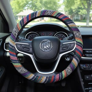 May include: A colorful steering wheel cover with a geometric pattern in shades of red, blue, green, and purple. The cover is wrapped around a black steering wheel with the Buick logo in the center. The car's dashboard is visible in the background.