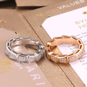 May include: Two rings with a segmented, geometric design. One ring is silver-toned metal and the other is rose gold-toned metal. Both rings feature small, clear, sparkling stones embedded in the outer segments of the band.