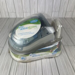 May include: A Febreze Scentstories player in a clear plastic retail package. The device is grey and blue with a label stating it circulates 5 complementary scents every 30 minutes. The packaging includes a disc and features green landscape imagery.