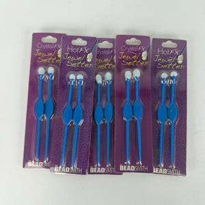 May include: Five packages of Crystal FX Jewel Setter tools by The Beadsmith. Each purple card holds two blue plastic applicators with white tips, designed for placing small embellishments. The packaging features the product name in white text.