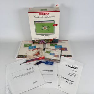 May include: A Bernina Embroidery Software Version 4 box set including two spiral-bound manuals, a CD-ROM case with a butterfly graphic, a blue USB dongle, and several printed support and installation notes on white paper with black text.