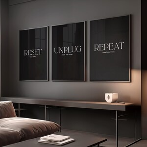May include: Three framed black art prints with white text. The prints read "RESET Your Mind", "UNPLUG From The Noise", and "REPEAT What Matters". The prints are displayed above a dark gray console table with a small white decorative object.