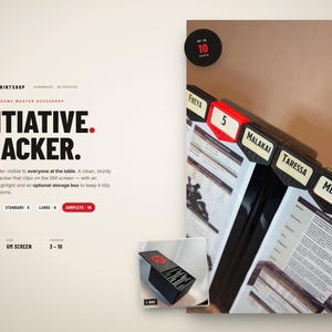 Könnte beinhalten: Ein Tabletop-Spielleiter-Zubehör, ein Initiative-Tracker, mit dem Text "INITIATIVE. TRACKER." Der Tracker wird an einem GM-Bildschirm befestigt und hebt die aktive Runde hervor. Das Bild zeigt eine schwarze Aufbewahrungsbox und Namensschilder.