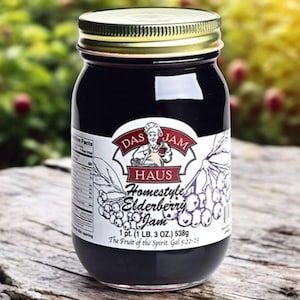 May include: A jar of Das Haus Homestyle Elderberry Jam. The label features an illustration of a chef and elderberry branches. The jar contains a dark purple jam and has a gold lid. The label reads "1 pt. (1 LB. 3 OZ.) 538g".