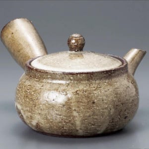 May include: A ceramic teapot with a rounded body, a lid with a small knob, and a spout. The teapot is a mottled beige and brown color, with a textured surface. The design is simple and functional.