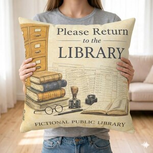 Può includere: Cuscino color crema con un tema di biblioteca vintage. Il cuscino presenta illustrazioni di libri, un catalogo e il testo "Please Return to the LIBRARY" e "FICTIONAL PUBLIC LIBRARY".