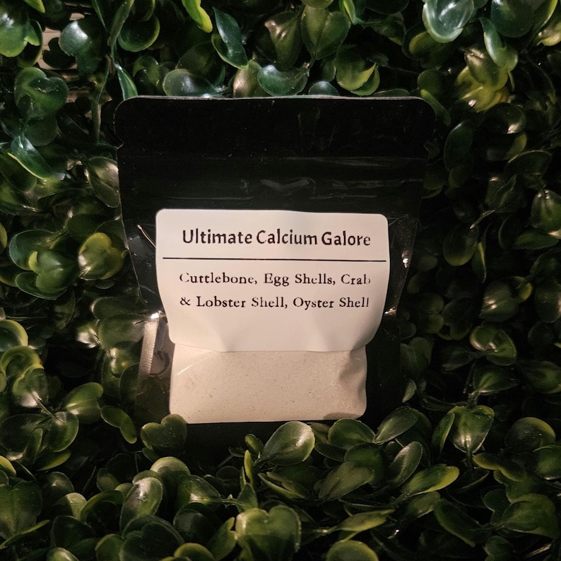 May include: A black resealable pouch containing a fine off-white powder. The white label reads: Ultimate Calcium Galore, Cuttlebone, Egg Shells, Crab & Lobster Shell, Oyster Shell. The pouch is filled with a calcium supplement powder mixture.