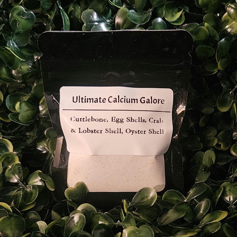 May include: A black resealable pouch containing a calcium supplement powder. The white label reads Ultimate Calcium Galore and lists the ingredients as Cuttlebone, Egg Shells, Crab & Lobster Shell, and Oyster Shell in black text.