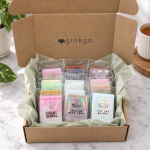 May include: A brown cardboard box containing multiple rectangular wax melts individually wrapped in clear plastic. The box lid features the ginkgo logo. The labels include text such as Strawberry Mix, Roasted Pine Cone, and The Tea Garden.