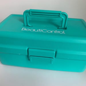 May include: A teal-colored, rectangular cosmetic case with a handle and a latch closure. The text "BeautiControl" is printed in white on the lid. The case is made of a solid, smooth material.