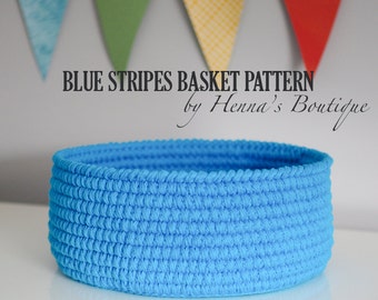 May include: A blue crocheted basket with a woven pattern. The basket is sitting on a white surface. The text "BLUE STRIPES BASKET PATTERN by Henna's Boutique" is above the basket.