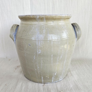 Pode incluir: Um pote de cerâmica bege com uma boca larga e duas alças laterais. O exterior apresenta um esmalte brilhante com padrões de gotejamento branco vertical e linhas horizontais gravadas na parte superior, com uma silhueta robusta.