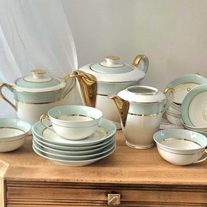 Peut inclure: Un service à thé en porcelaine composé d'une base blanche avec des bandes vert menthe pâle et des bordures dorées. L'ensemble comprend une théière, un sucrier avec couvercle, un pot à lait et plusieurs tasses avec soucoupes assorties.