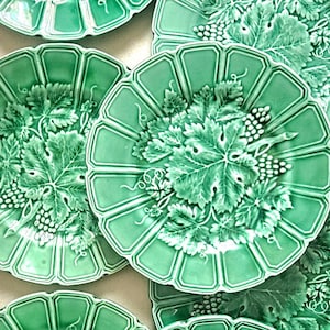 Peut inclure: Un ensemble d'assiettes rondes en céramique vert vif présentant un motif en relief de grappes de raisin, de feuilles de vigne détaillées et de vrilles. Chaque assiette possède un bord festonné et cannelé avec une finition brillante.