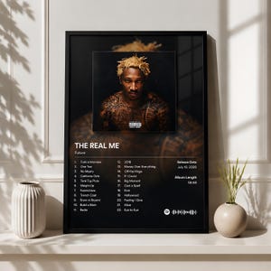 Peut inclure: Une affiche noire encadrée présentant le portrait d'une personne aux cheveux blonds et tatouée, intitulée The Real Me de Future. L'affiche comprend une liste de 22 chansons, une date de sortie du 10 juillet 2026, une durée de 58:56 et un code Spotify.