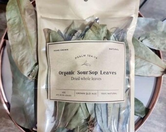 Op de afbeelding: Een transparante zak gevuld met gedroogde groene bladeren. Het etiket luidt "Organic SourSop Leaves, Dried whole leaves". Het etiket bevat ook de tekst "Home Grown", "Psalm 104:14" en "100% Natural".
