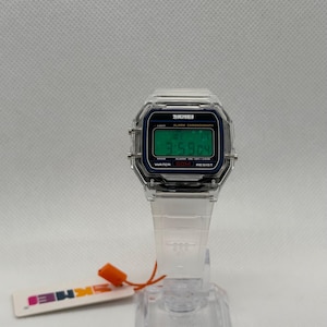 K&ouml;nnte beinhalten: Transparente Digitaluhr mit rechteckigem Zifferblatt und transparentem Armband. Das Zifferblatt zeigt die Uhrzeit in gr&uuml;nen Ziffern an. Die Uhr hat den Markennamen "SKMEI" auf dem Zifferblatt. Ein kleines Etikett mit dem Markennamen ist angebracht.