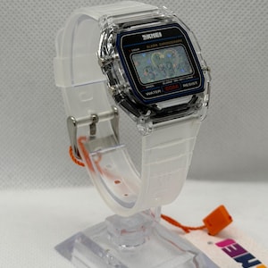 May include: A digital wristwatch with a clear, transparent resin case and matching translucent white silicone strap. The rectangular watch face features a black border, a digital display with the text SKMEI, ALARM CHRONOGRAPH, and WATER 50M RESIST.