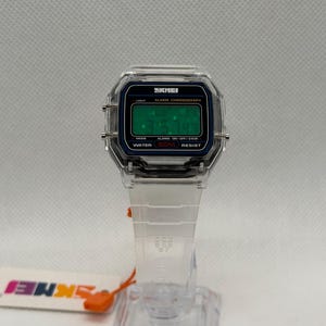 K&ouml;nnte beinhalten: Transparente Digitaluhr mit rechteckigem Zifferblatt und transparentem Armband. Das Zifferblatt hat einen schwarzen Rand mit dem Text "SKMEI" und eine gr&uuml;ne Digitalanzeige. Armband und Uhrengeh&auml;use sind transparent.