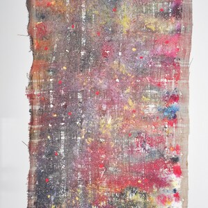 May include: Abstract textile art piece with a rectangular shape. The artwork features a blend of colors, including red, yellow, purple, and blue, with a textured, woven appearance. The edges are frayed, and the piece is mounted on a white background.