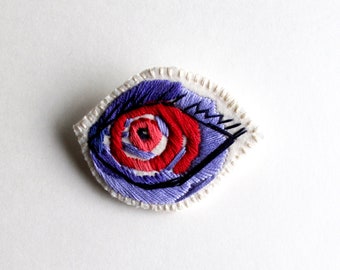 Hand embroidered abstract eye brooch using purples and reds on bright cream muslin and cream felt An Astrid Endeavor Summer fashion