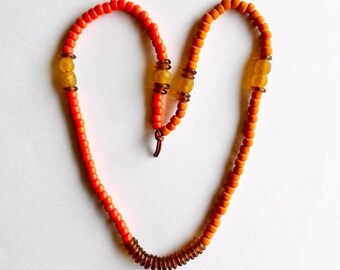 Long asymmetrical orange necklace with glass beads from Ghana and Native American Crow beads on silver leather cord statement jewelry