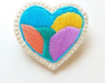Hand embroidered heart brooch with geometric design with peach, blue, purple, green and yellow on cream muslin An Astrid Endeavor gift idea