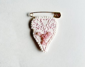 Embroidered heart brooch with light pink thread and rose quartz beads on bright cream muslin with cream felt back on gold tone safety pin