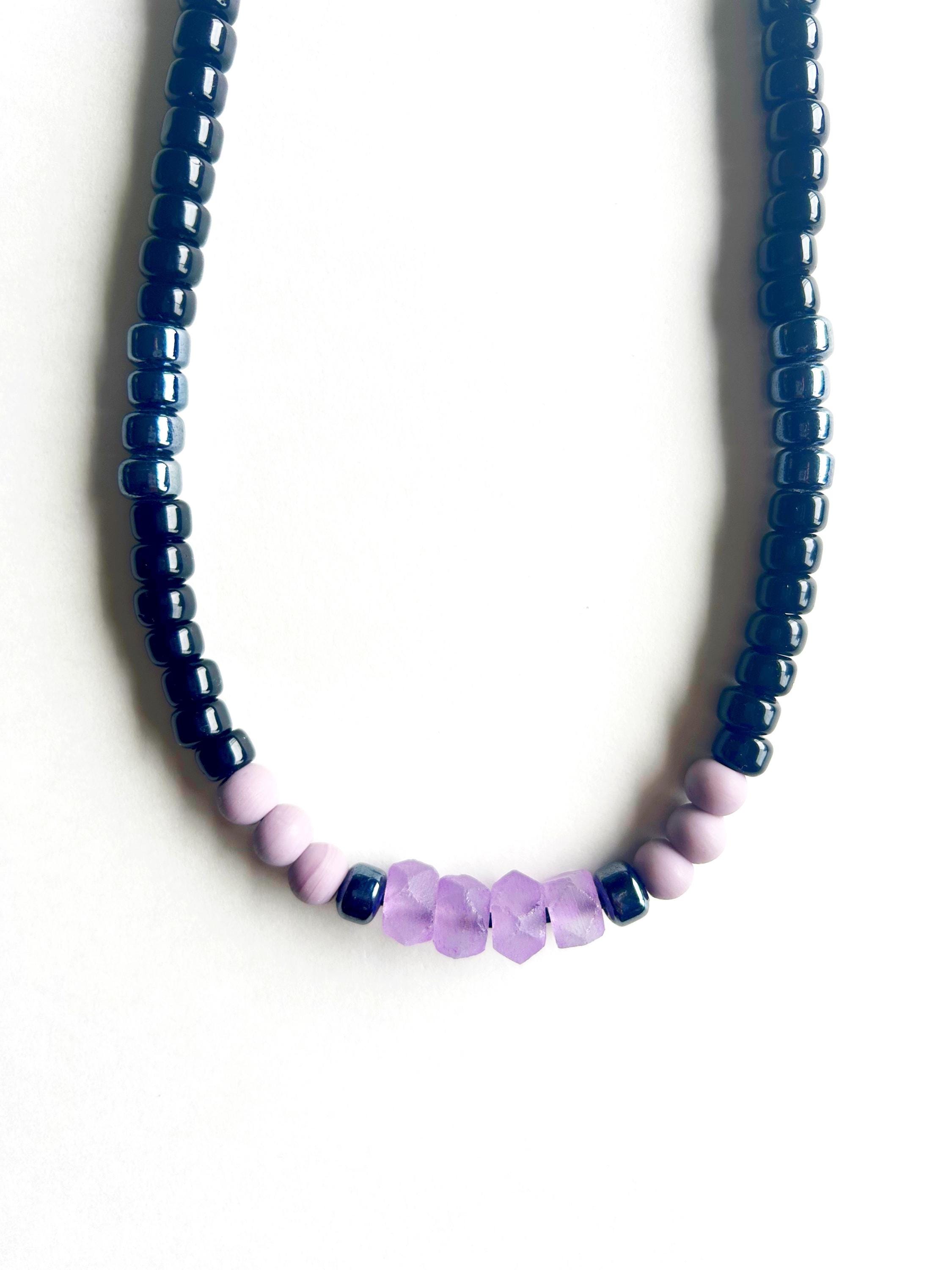 Beaded necklace with black and gunmetal gray colors with lavender and purple beads at focal point on black leather cord An Astrid Endeavor