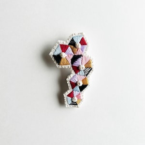 Hand embroidered brooch geometric design using pink lavender tan maroon blue black threads with shell beads An Astrid Endeavor fiber jewelry