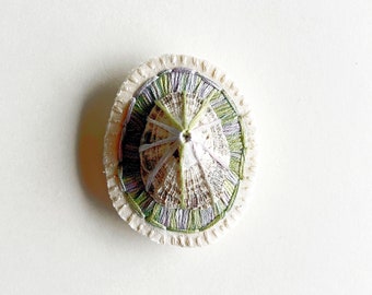 Hand embroidered brooch abstract design using lavender and green variegated threads and limpet shell An Astrid Endeavor fiber jewelry