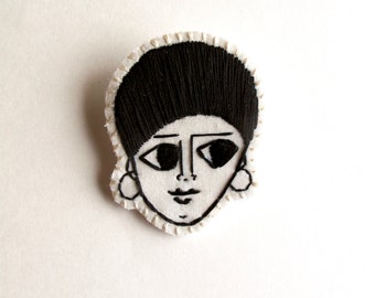 Hand embroidered brooch with Ethiopian inspired woman's face on cream muslin with black thread cream felt backing An Astrid Endeavor