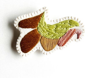 Hand embroidered brooch with unique abstract design using pale green tan and variegated peach thread An Astrid Endeavor textile jewelry