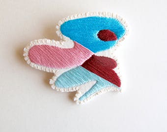 Hand embroidered brooch with unique geometric design using blues, pink and maroon cotton thread An Astrid Endeavor textile jewelry